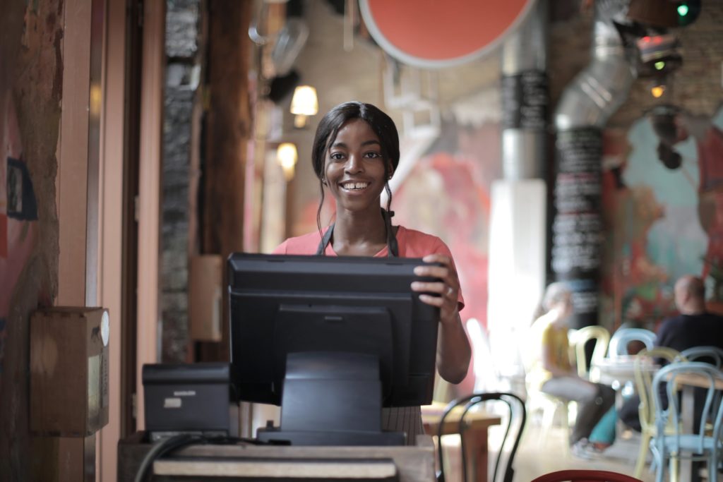 cheerful black waitress using POS at restaurant