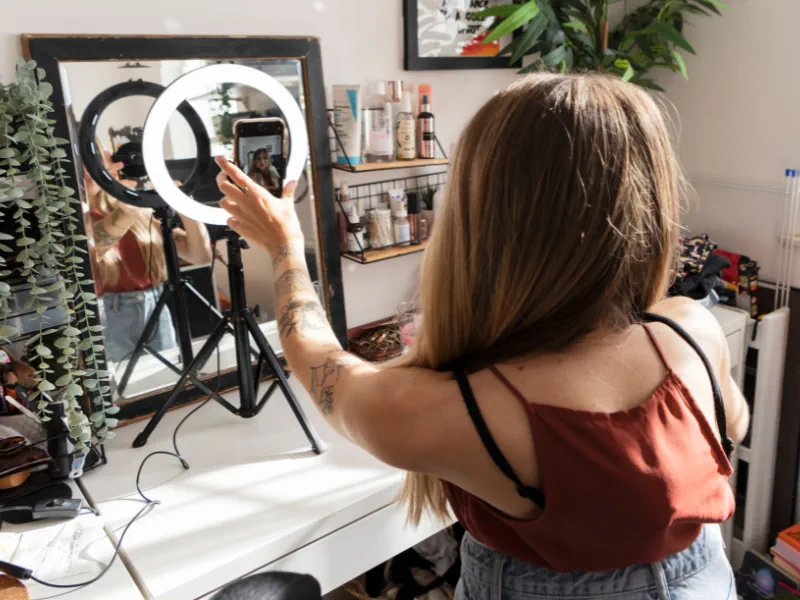 woman taking selfie video with ring light sitting at desk with plants and beauty products